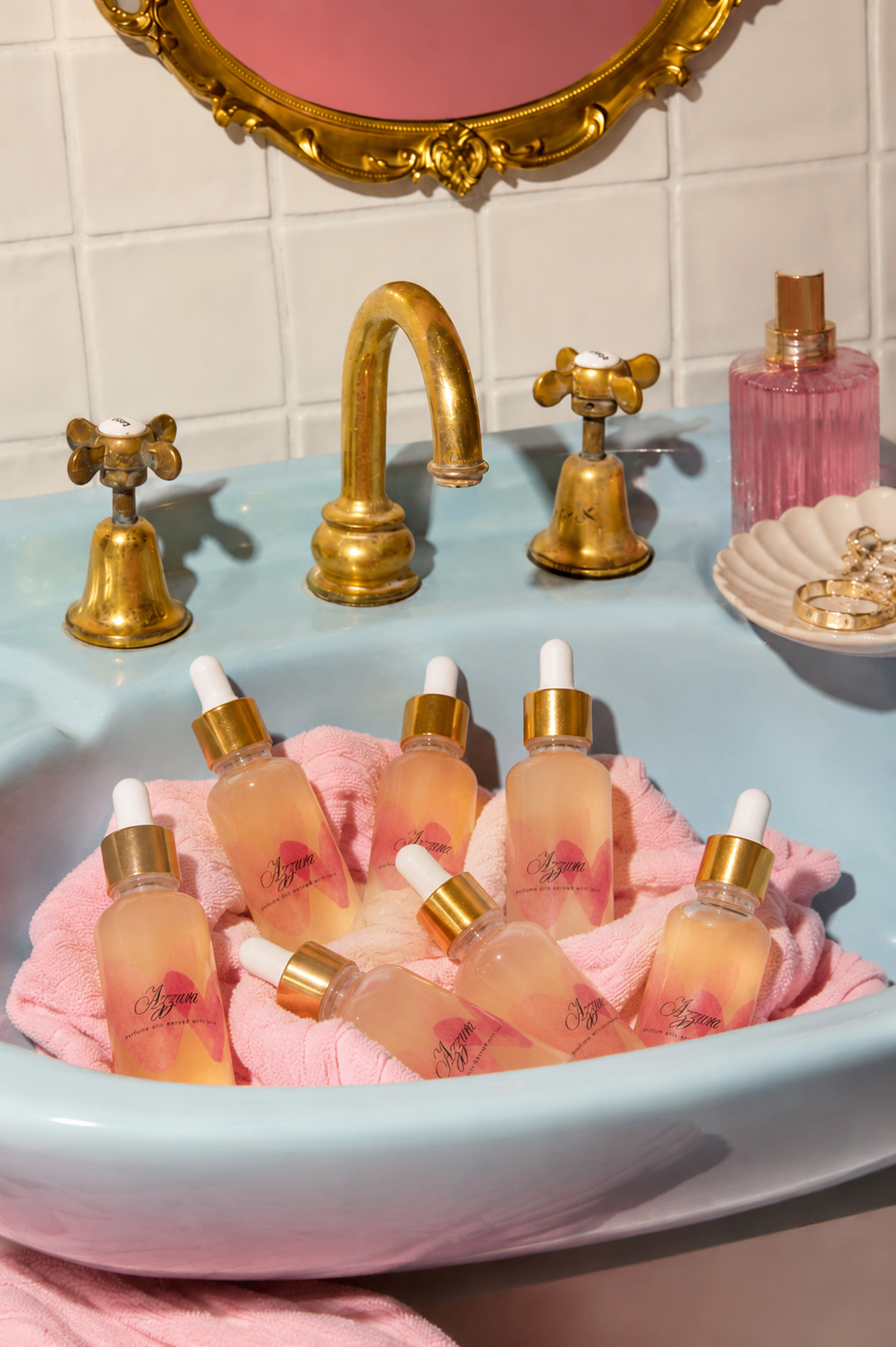 Azzura perfume oil bottles nestled on a soft pink towel in a vintage blue basin with brass fixtures